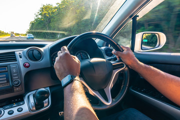 Both hands of young black adult male on steering wheel driving right hand drive vehicle on left side of road - Powered by Adobe