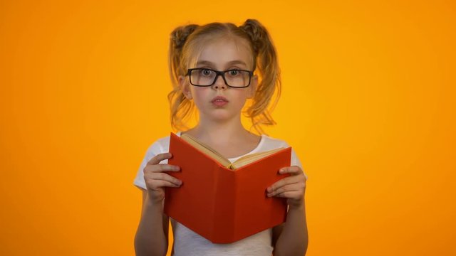 Surprised nerd girl in eyeglasses hiding behind book, interesting story, genius