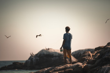 Obraz premium The kid on the cliff staring at the ocean and the seagull in the horizon