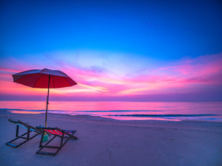 Sunrise with dramatic morning sky over sea with chair and umbrella on beach