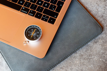 Rose-gold laptop keyboard and compass. Internet navigation or travel and online booking concept.