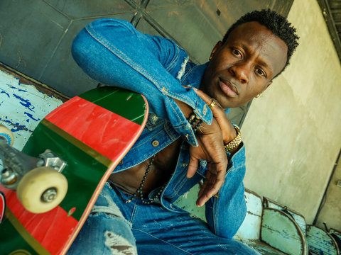 young attractive and fit black afro American man sitting on corner street bench holding skate board posing in cool attitude in youth urban style and city lifestyle