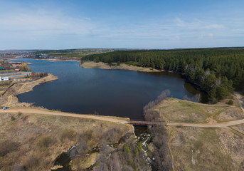 Fototapeta premium A pond in the Gileva village, a dam, a road bridge and a small waterfall. Sunny, spring, Aerial.