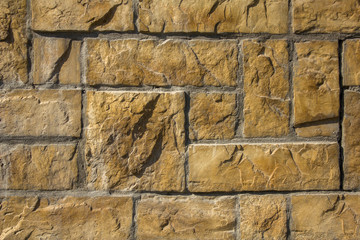 concrete wall of yellow stone square and rectangular bricks of different sizes in gray cement. rough surface texture