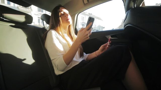 beautiful lady travels on car back leather seat holding smartphone in hand in sunny weather