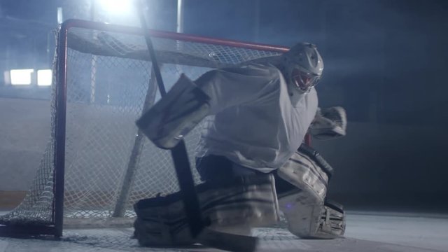 Male hockey goaltender training on ice rink, he is trying to stop puck from entering net but failing to catch it
