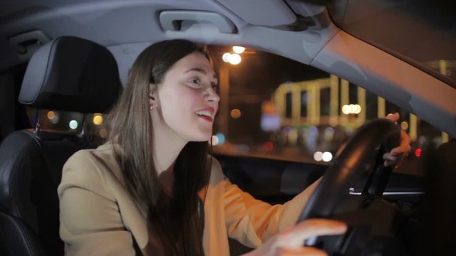 tremendous brunette with long loose flowing hair drives car and smiles admiring night city lights close view