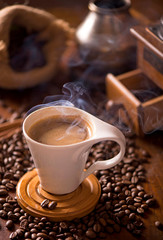 cup of coffee and coffee beans in a sack on dark background, top view