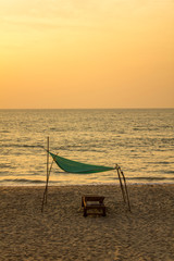 empty wooden beach bed on the yellow sand under a green canopy against the ocean and the evening sunset sky