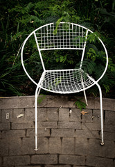 An empty white metal garden chair isolated against dark foliage background outdoors image in portrait format with copy space