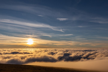 Beautiful sunset over a valley filled by fog with mountains and hills