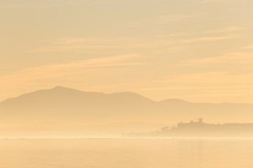Beautiful view of Trasimeno lake at sunset with birds on water and Castiglione del Lago town