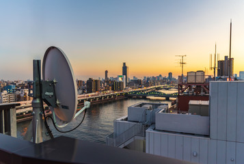 Satellte dish at the top of building at sunset with a background of Sumida river and Tokyo city.