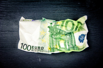 100 euro crushed banknote on a black wooden background