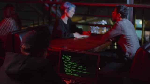 Rare view of hacker sitting in caf&eacute; at laptop and coding