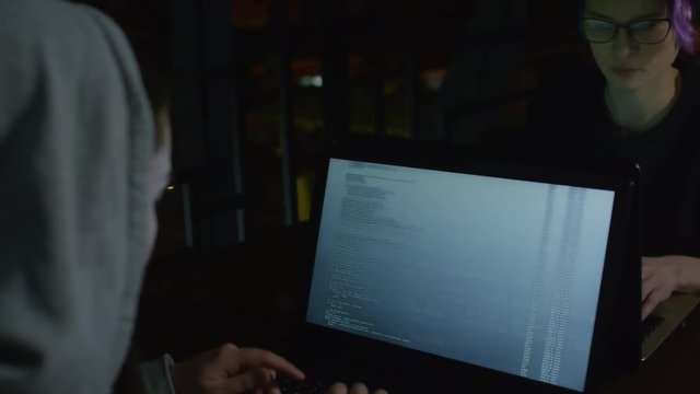 Back view of two young Caucasian women in hoodie sitting at table in front of each other and developing program code together