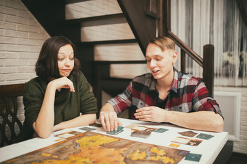Couple sitting at the table. Young People having fun while playing board game.