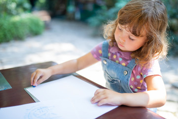 Cute toddler girl drawing with chalk pencils outdoors