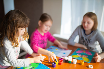 Fototapeta premium Three sisters little girls drawing with fingers on paper. Play, fun, childhood. Montessori school