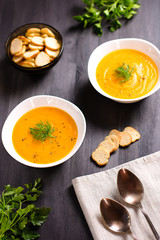 Pumpkin cream soup with croutons and fresh dill and parsley on dark wooden background, top view