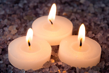 preparations for the bath and aromatherapy : three decorative candle stand in aromatic sea salt with smell of lavender in the shadows