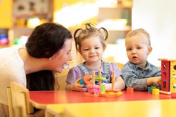 cute babies play with carer or babysitter in nursery or kindergarten