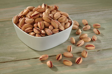 Pistachios in white bowl on wooden background