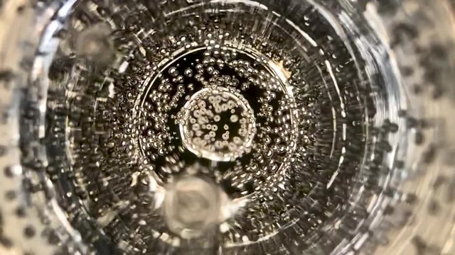 Slow motion and extreme close up shot of a glass of champagne bubbles moving up to the surface and exploding.