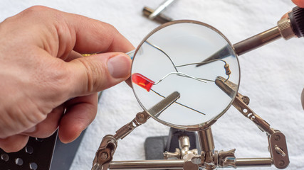 Soldering a resistor and LED with a magnifying glass, with alligator clips holding the components