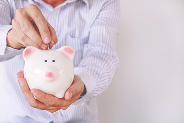 Close-up of a businessman putting a coin into a piggy bank against a white background .