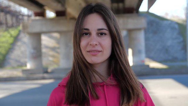 Portrait of a beautiful woman in a raspberry sweatshirt on the background of the city under the bridge. 4k