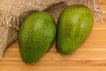 Two whole green avocado fruits on a wooden surface