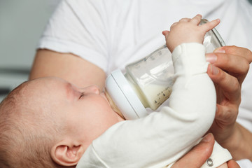 Baby drinking milk from glass bottle holding by father. Healthy nutrition