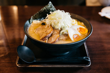 Ramen Pork Bone Soup (Tonkotsu Ramen) with Chashu Pork, Scallion, Sprout, Corn, Dried Seaweed and boiled egg served in black bowl.