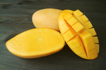 Fresh Ripe Thai Nam Dok Mai Mangoes Whole Fruit and Cut in Half on Dark Brown Wooden Background