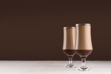 Creamy coffee cocktail in two elegant glass with chocolate on white table and dark brown wall.