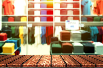 Wooden table with blurry background of casual boutique shop, shirt brand outlet or colorful clothes store for product display montage. Retail business of fashion product for online marketing backdrop.