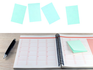 open notebook with sticky notes and black ballpoint pen on wooden table and blue blank paper notes levitating isolated on white background, closeup diary calendar for business or education planning