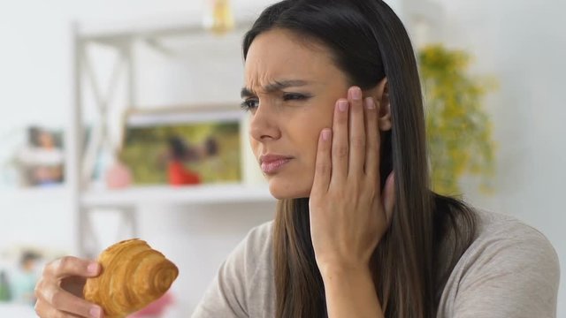 Girl biting croissant and feeling unpleasant pain, tooth and gum sensitivity
