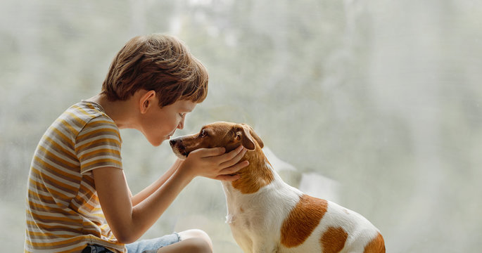 Child kisses the dog in nose on the window.