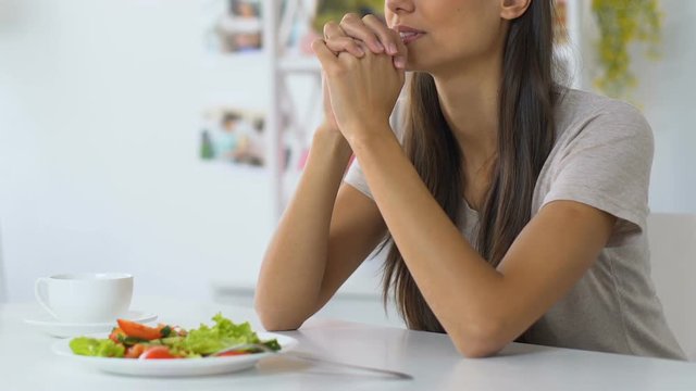 Young woman praying before eating, asking god to bless food, faith, christianity