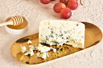 Fresh blue cheese on a golden saucer, honey and grapes.