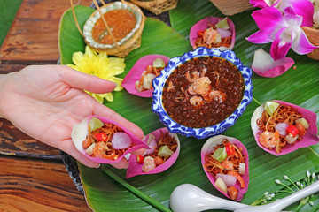 Woman's Hand Holding a Fresh Lotus Petal Savory Wrapped Called Miang kham in Thai Language 