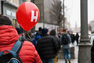 Just a man walking down the street with a red balloon.