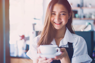 Pretty young asian waitress standing arms crossed in cafeteria.Coffee Business owner Concept.  barista in apron smiling at camera in coffee shop counter