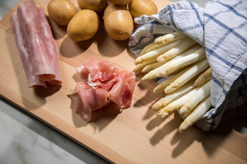 Roher, weißer Spargel in Tuch mit Kochschinken, geräucherten Schinken und Kartoffeln auf Holz...