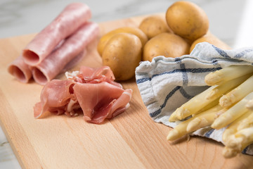 Roher, weißer Spargel in Tuch mit Kochschinken, geräucherten Schinken und Kartoffeln auf Holz Brett und Marmor Hintergrund