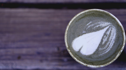 Cup of matcha tea with latte with heart on wooden background. Blurred background, place for text.