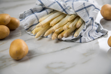 Roher, weißer Spargel in Tuch und Kartoffeln auf Marmor Hintergrund