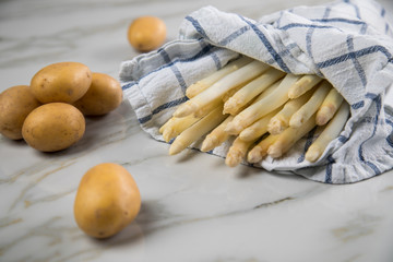 Roher, weißer Spargel in Tuch und Kartoffeln auf Marmor Hintergrund